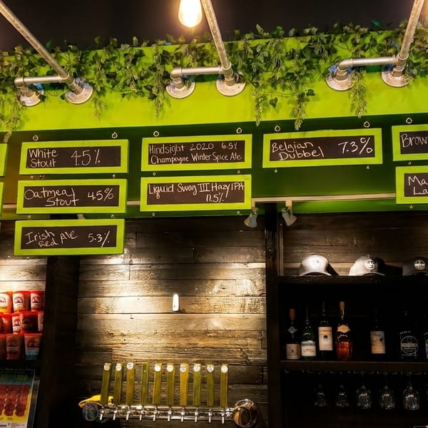 A brewery taproom with a chalkboard menu displaying various beers, taps, and merchandise.