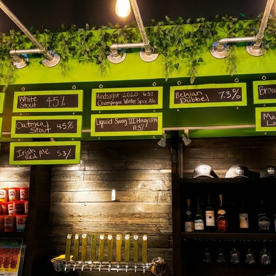 A brewery taproom with a chalkboard menu displaying various beers, taps, and merchandise.
