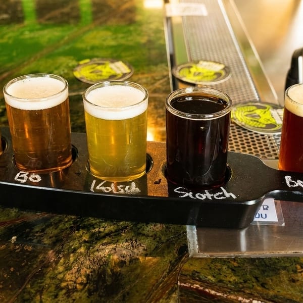 A black paddle holds five glasses of beer, ranging from light to dark, on a green marble bar.
