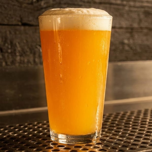 A tall glass of golden beer with a frothy white head sits on a metal grate.