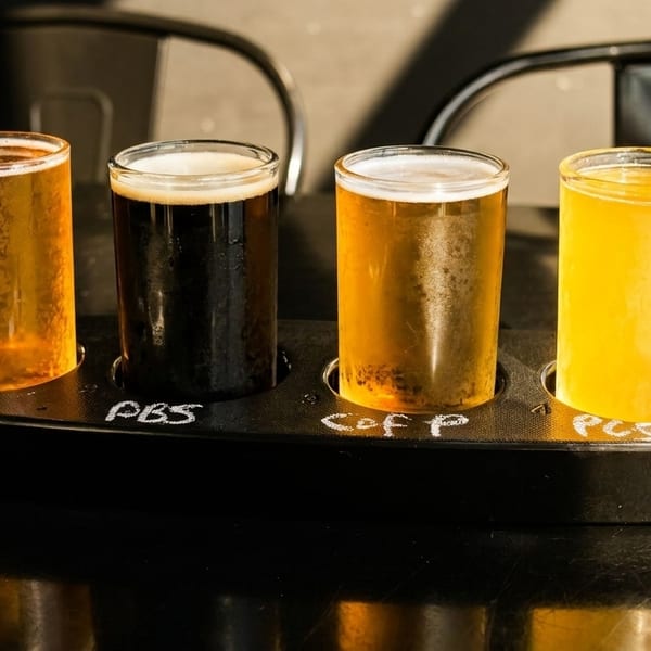 A four-glass beer flight with light and dark beers on a black table.